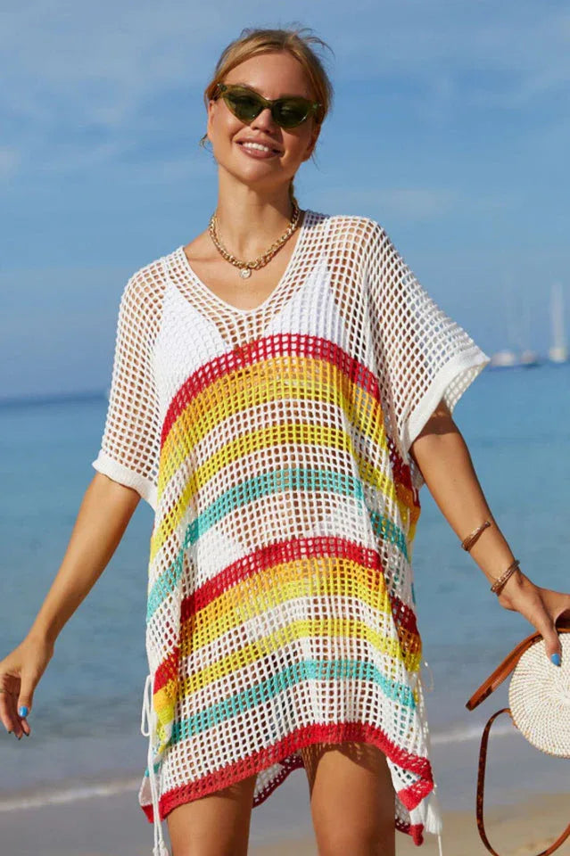 Woman wearing a white and striped mesh knit tunic over a white bikini on a beach.