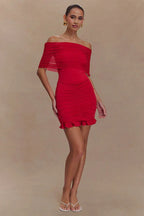Side view of a woman in a red off-the-shoulder ruched mini dress with a sheer overlay and ruffled hem.
