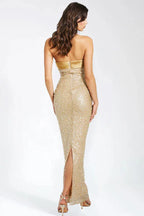 Back view of a woman in a gold floor-length strapless gown with a high slit.