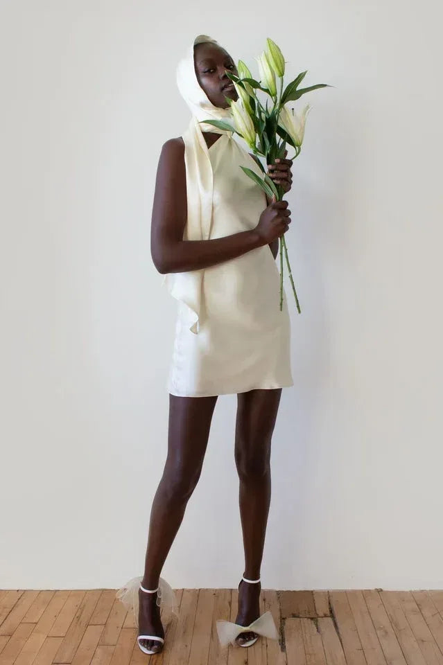 woman wearing a cream-colored satin mini dress with a halter neckline, holding lilies