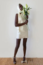 woman wearing a cream-colored satin mini dress with a halter neckline, holding lilies