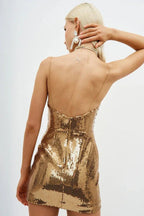 Back view of a woman in a gold sequined mini dress with spaghetti straps and a low back.