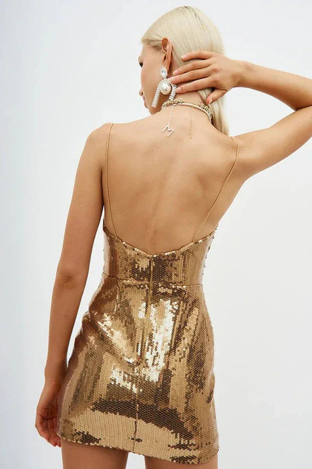 Back view of a woman in a gold sequined mini dress with spaghetti straps and a low back.
