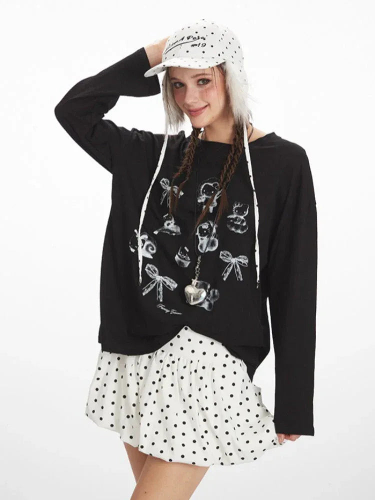 Woman in a black long-sleeved graphic t-shirt and white polka dot skirt smiling and touching her hat.