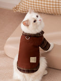 A white cat wearing a brown plaid pet shirt, showing the back and D-ring leash attachment.