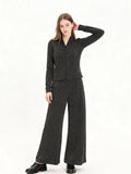 Woman wearing a charcoal grey knit loungewear set with a full zip jacket and wide leg pants, posing with hand on head.