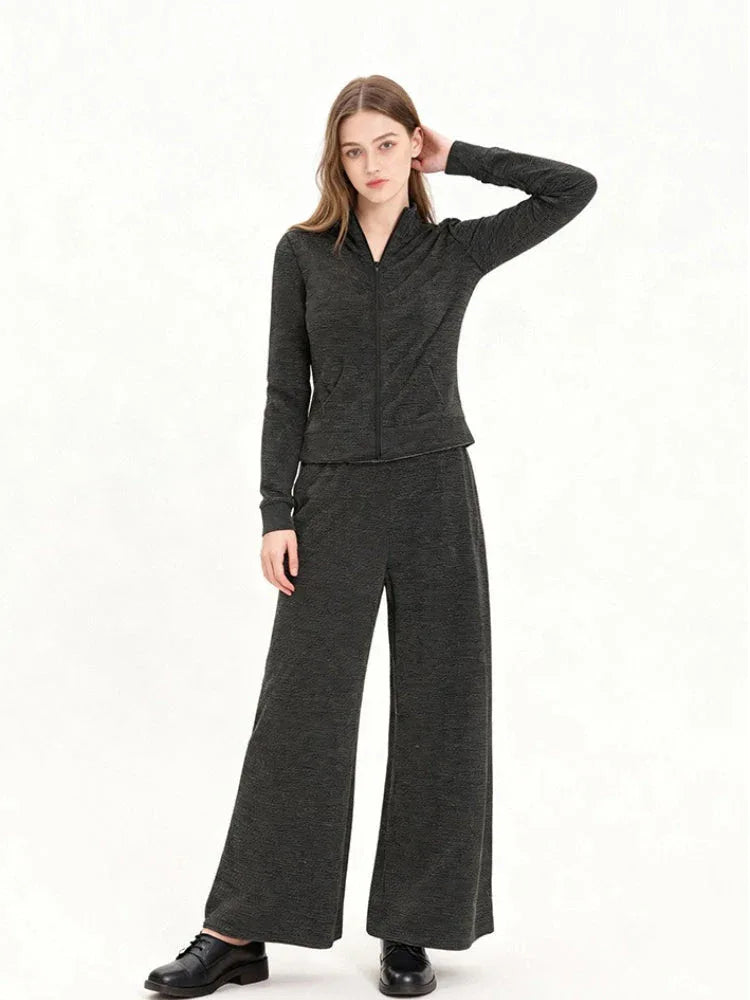 Woman wearing a charcoal grey knit loungewear set with a full zip jacket and wide leg pants, posing with hand on head.