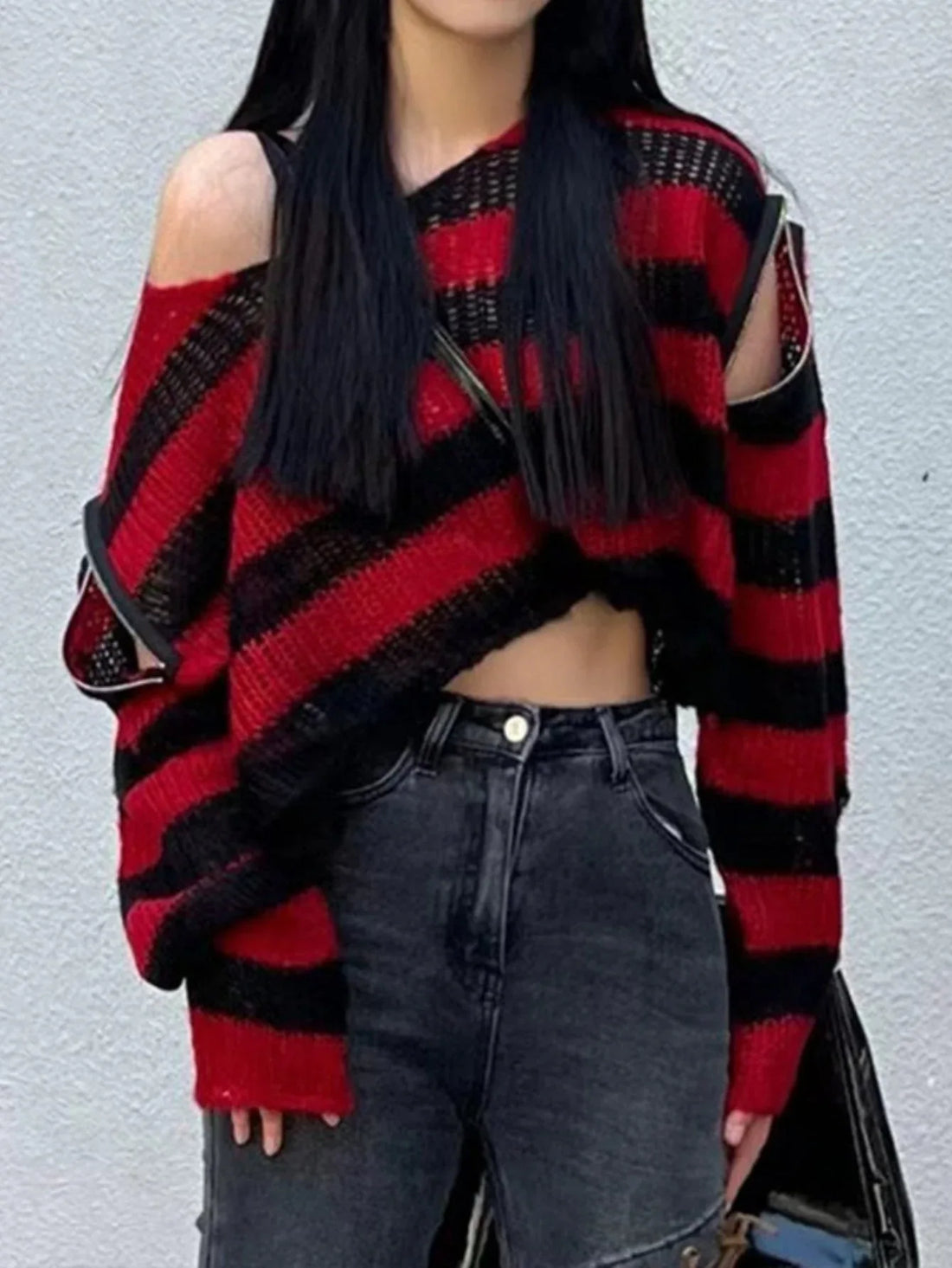 Woman wearing a red and black striped cropped knit sweater with cut-out shoulders and zippered sleeves.