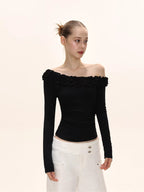 Close-up of a woman wearing a black long-sleeved ruffled off-the-shoulder top.