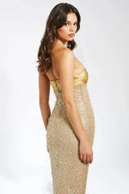 Side view of a woman in a gold strapless beaded and sequined gown.