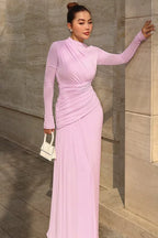 Woman in a lavender long-sleeved draped maxi dress with a white handbag.