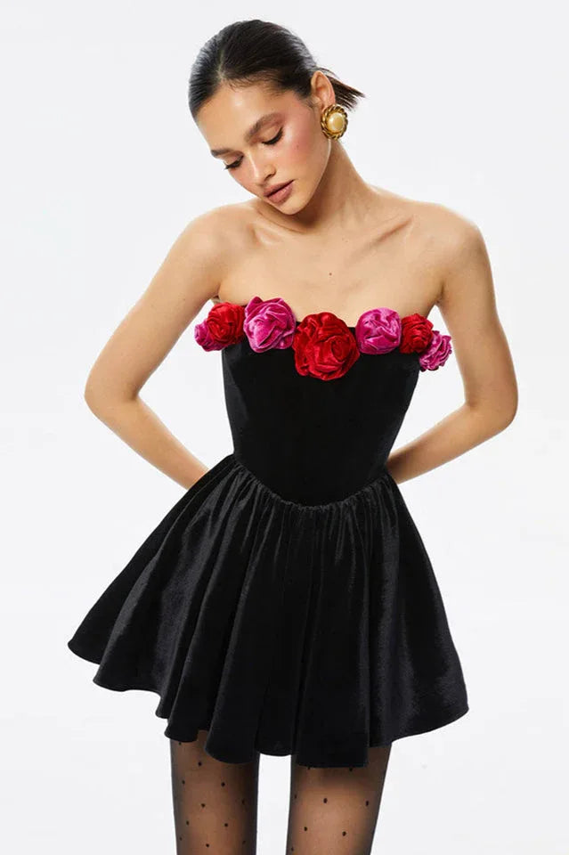 Model wearing a black strapless velvet mini dress with a floral trim at the neckline and a full skirt.