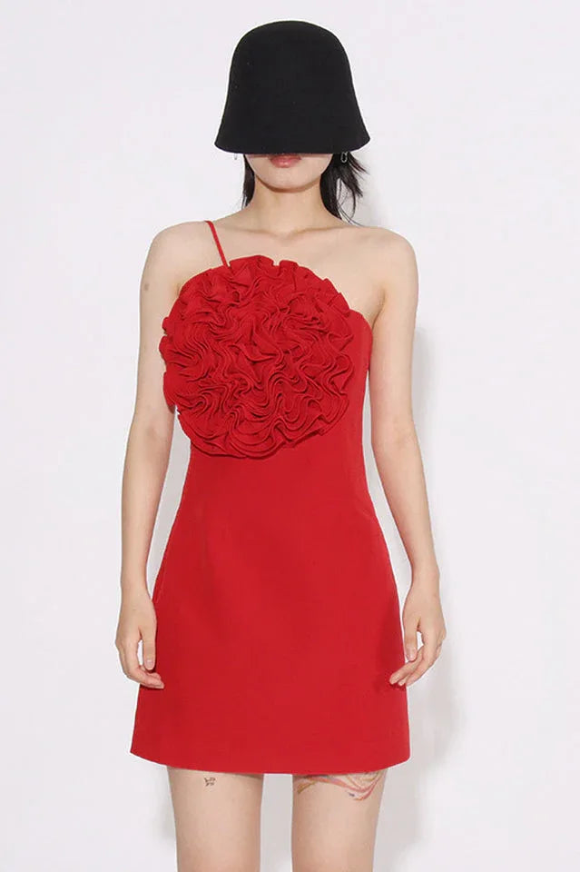 Woman wearing a red one-shoulder sheath dress with a large floral applique on the bust and a black bucket hat