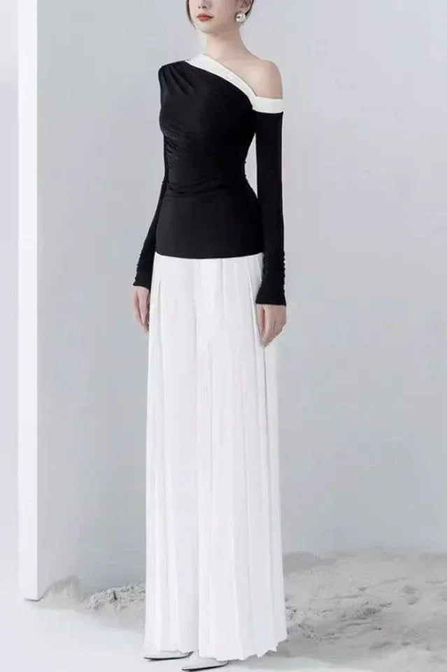 Side profile of a woman in a black and white outfit featuring an asymmetrical top and pleated trousers.