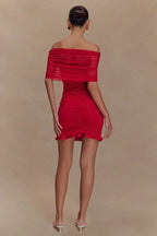 Full body shot of a woman posing in a red off-the-shoulder ruched mini dress with a sheer overlay.