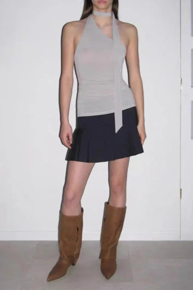 Model wearing a light gray halter top, black pleated mini skirt, and brown knee-high boots.