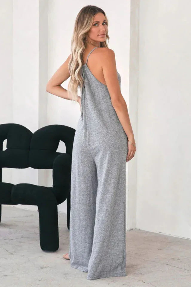 Back view of a woman in a grey jersey knit wide leg jumpsuit with patch pockets and spaghetti straps.