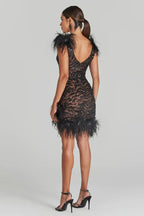 Back view of a woman in a short black sequined dress with feather trim and a v-shaped back.