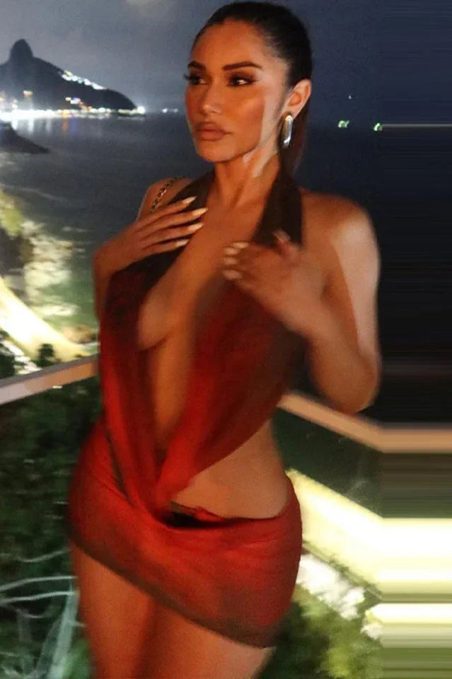 Model posing in a red and black printed halter mini dress at night