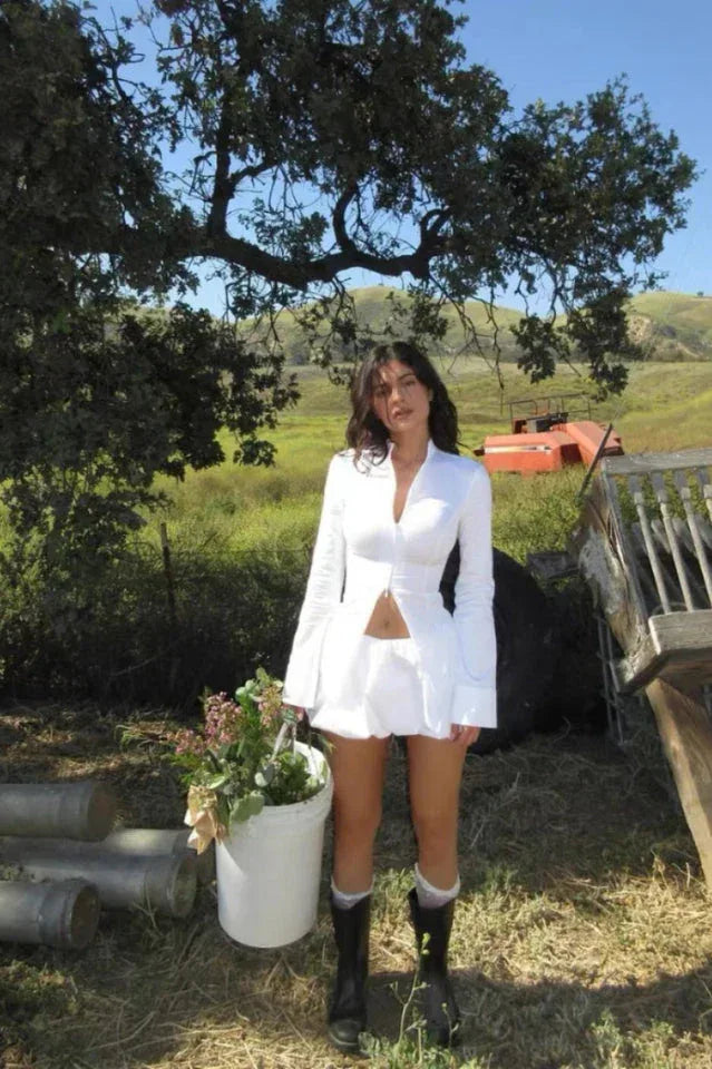 Woman in a white outfit standing in a field with a bucket of flowers