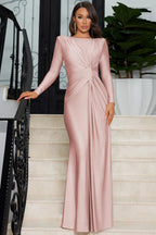 Woman in a long-sleeved, ruched pink satin gown standing on stairs.