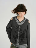 Woman with hair blowing slightly, wearing a dark gray graphic print cropped long-sleeve top with cold shoulder cutouts and a lace-up front over a gray and white striped t-shirt.