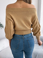 Back view of a woman wearing a tan off-the-shoulder cable knit cropped sweater and blue jeans.