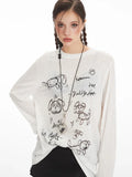 Front view of a woman wearing a white long-sleeve sheer knit t-shirt with a black dog graphic print and text, and a silver heart pendant necklace.