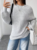 Woman taking a selfie while wearing a light grey oversized knit sweater and blue denim jeans, accessorized with a black handbag.