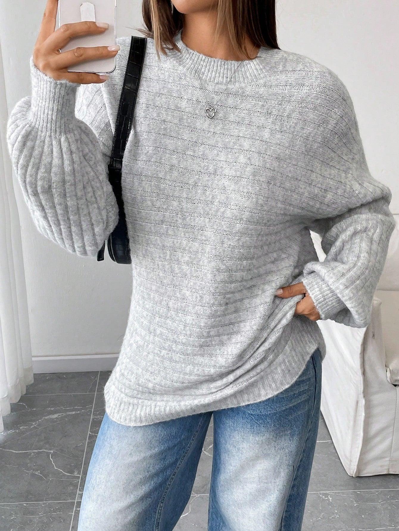 Woman taking a selfie while wearing a light grey oversized knit sweater and blue denim jeans, accessorized with a black handbag.