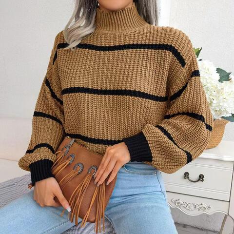 Woman wearing a tan and black striped knit mock neck sweater and light wash denim jeans, holding a tan fringe handbag