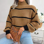 Woman wearing a tan and black striped knit mock neck sweater and light wash denim jeans, holding a tan fringe handbag