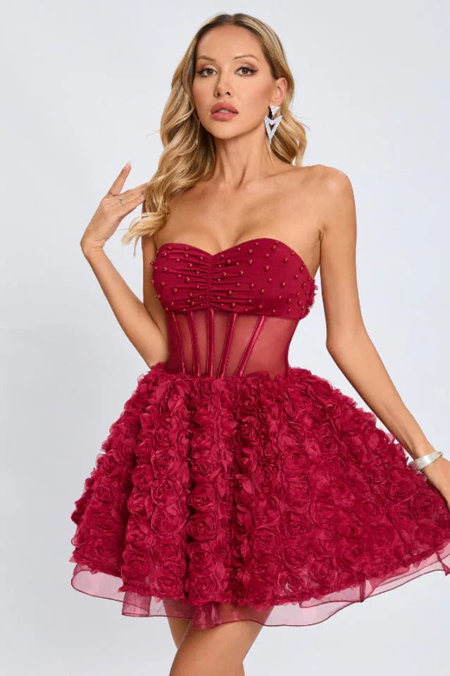Close-up of a woman in a strapless red dress featuring a ruched and beaded bodice and a skirt made of fabric roses.