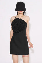 Woman wearing a black one-shoulder sheath dress with a large floral applique on the bust and a black bucket hat