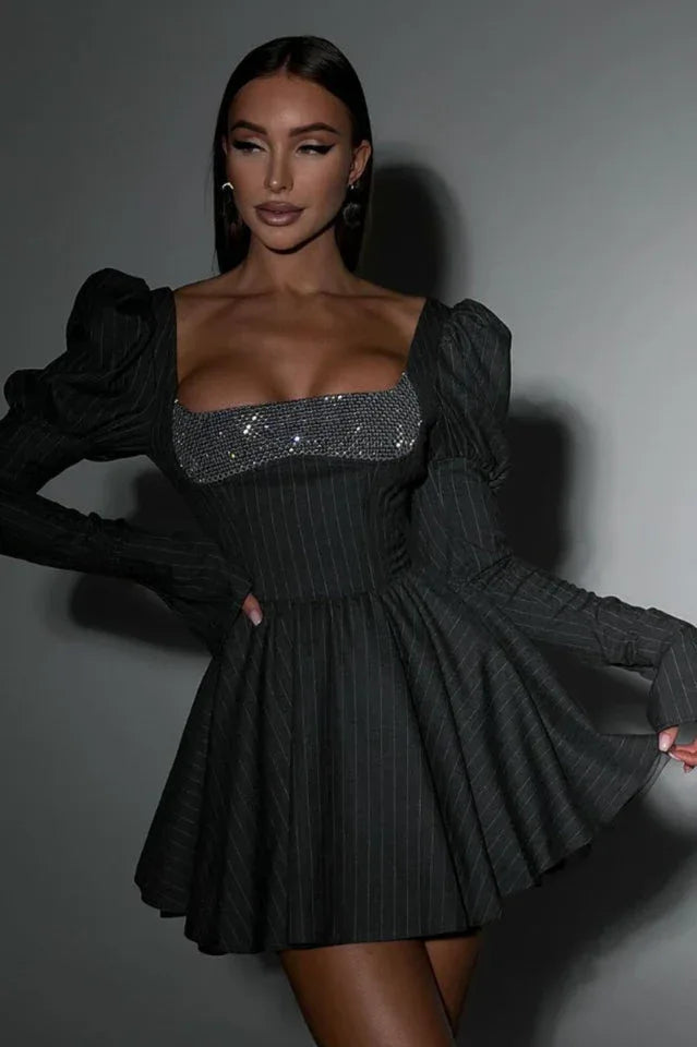 Woman wearing a dark grey pinstripe mini dress with a sparkling square neckline and long puff sleeves, posing against a grey backdrop.