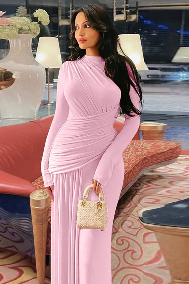 Woman in a long-sleeved pink draped dress holding a light-colored handbag.