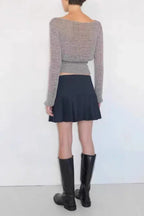 Back view of a model wearing a gray long-sleeve sweater, black pleated mini skirt, and black knee-high boots.
