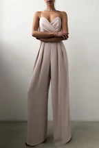 Woman in a beige satin jumpsuit with pleated wide legs and crossed arms