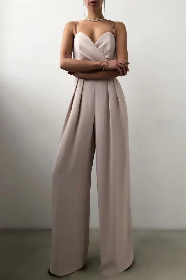 Woman in a beige satin jumpsuit with pleated wide legs and crossed arms