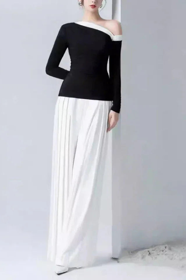 Back view of a woman modeling a black asymmetrical top and white pleated wide-leg pants.