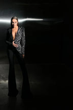 Woman posing in a black jumpsuit with a deep V-neck and flared legs in a dark setting.