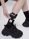 Black crew socks with a black and white cartoon cat character applique on the side, worn with black chunky sneakers.