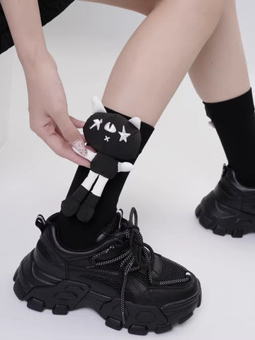 Black crew socks with a black and white cartoon cat character applique on the side, worn with black chunky sneakers.