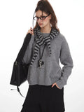 Close-up of woman in gray knit sweater with striped hood, black handbag, and pendant necklace