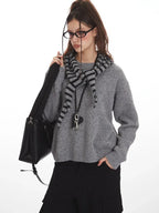 Close-up of woman in gray knit sweater with striped hood, black handbag, and pendant necklace