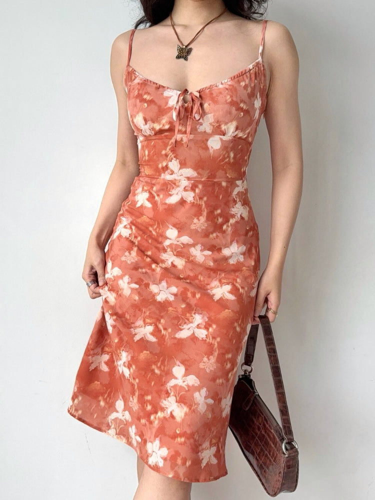 Woman posing with hands on hips in an orange floral print midi dress.