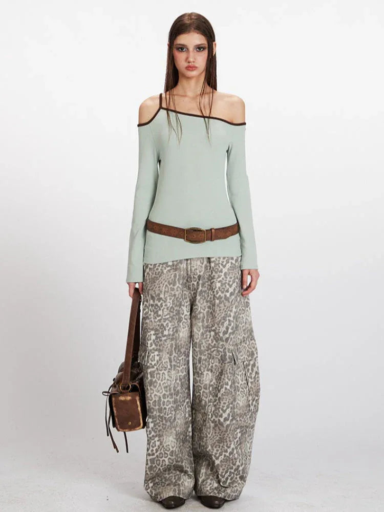 Model wearing a light green ribbed knit one-shoulder long sleeve top with dark trim, paired with leopard print pants and a brown belt.
