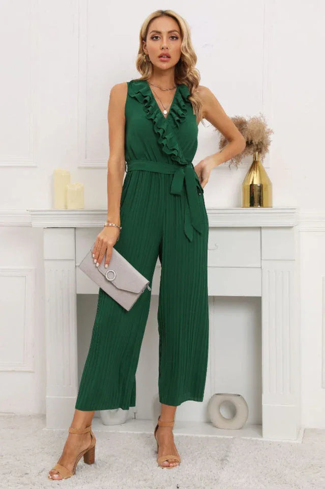 Woman wearing a green sleeveless pleated jumpsuit with a ruffled V-neck and a tie belt.