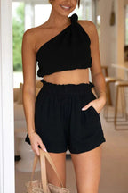 Woman wearing a black one-shoulder crop top and black ruffled shorts set