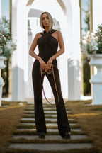 Woman in black flared leg jumpsuit with halter neckline and handbag